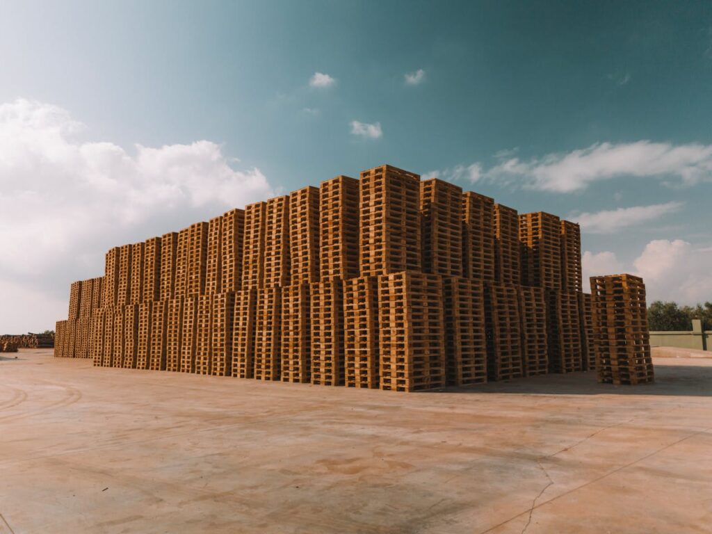 pexels photo 29982234 Large stacks of wooden pallets under a partly cloudy sky on a sunny day.